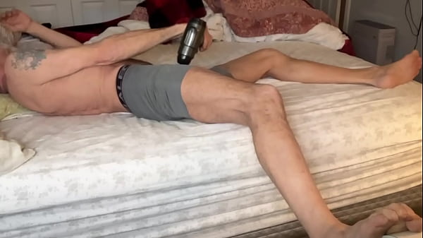 Image Stretching Tension in Bed with Massage Gun in on Bed in Tight Boxer Briefs July 2024